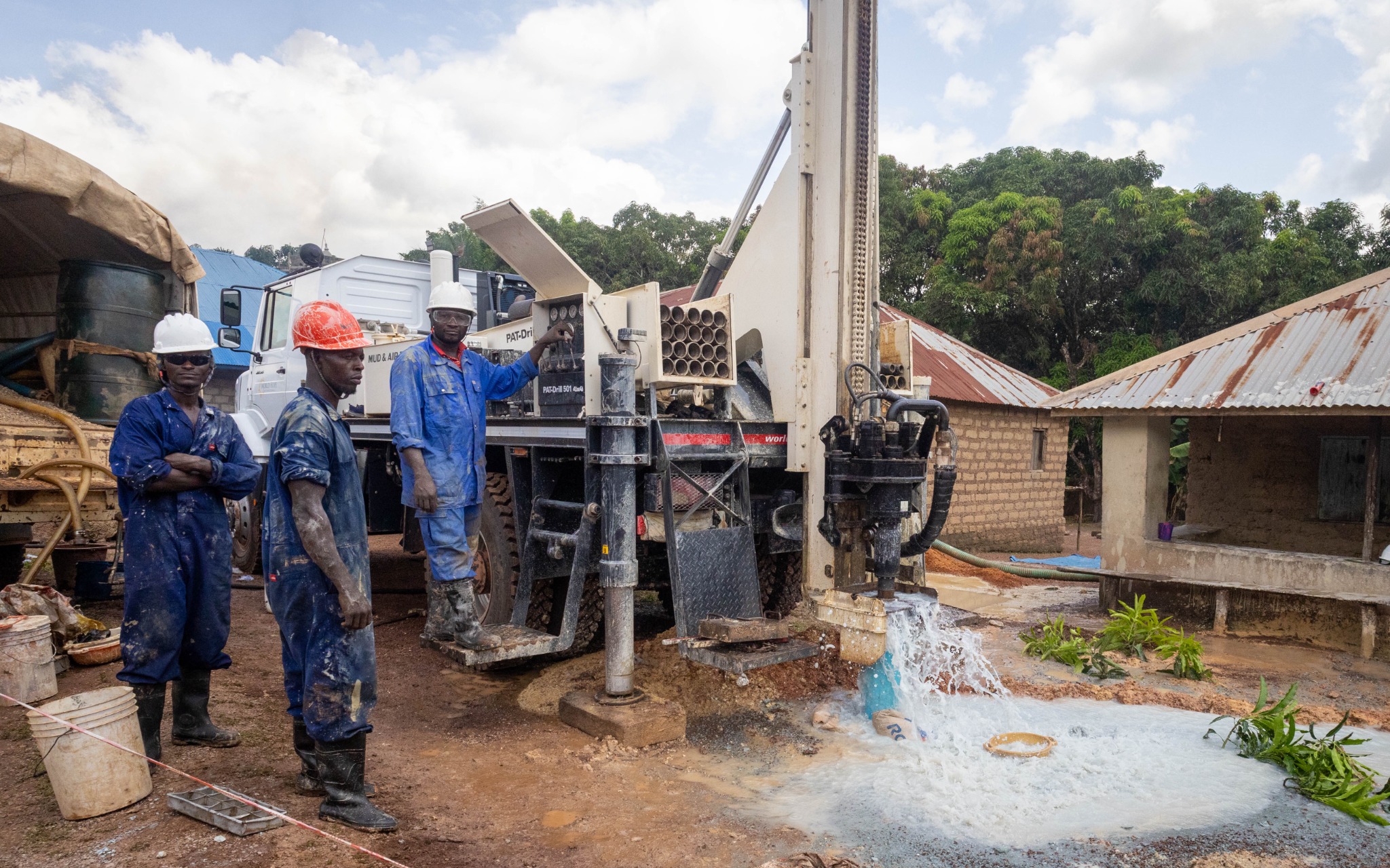 Three Sierra Leone drilling team members beside a well rig as clean water flows from the bore hole