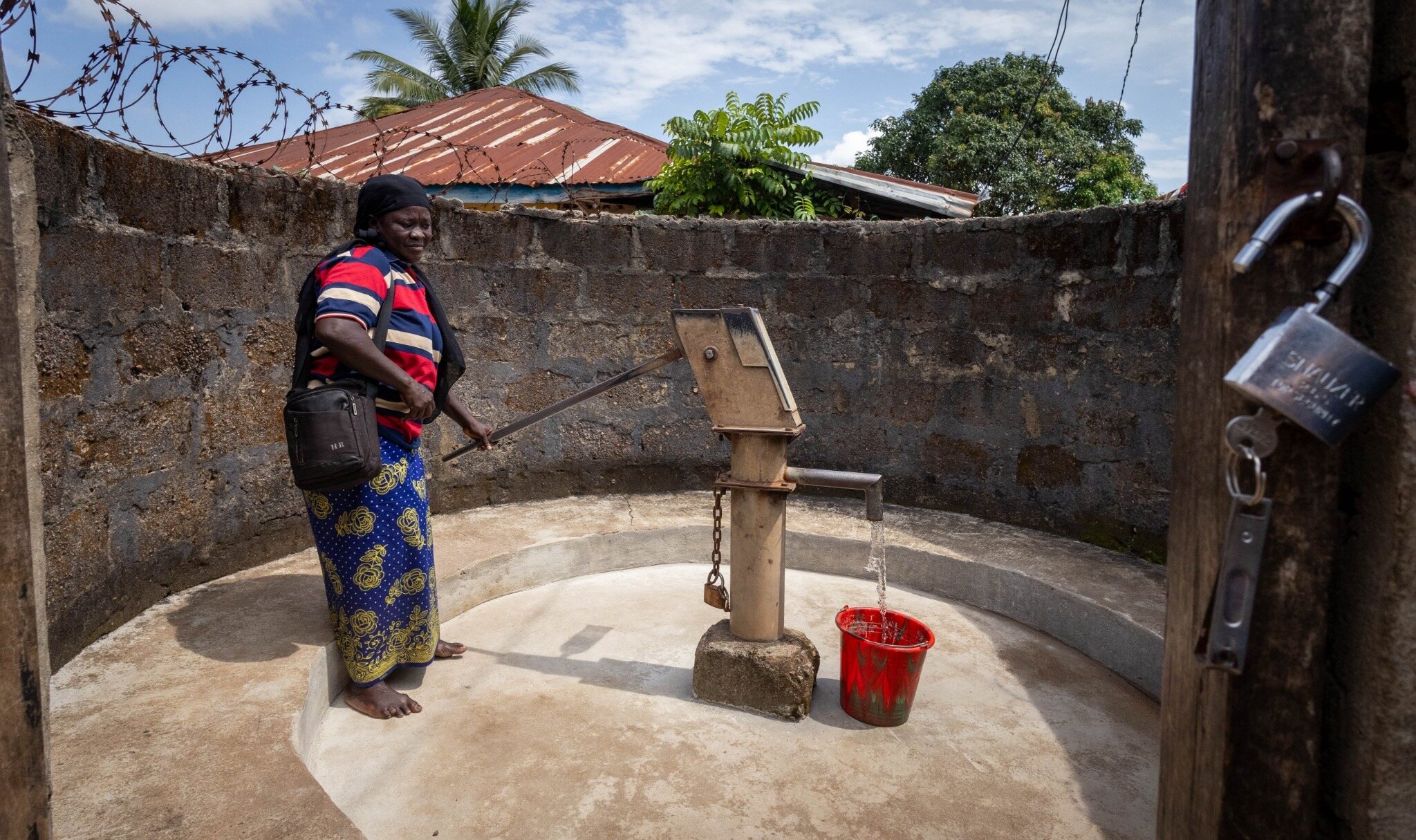 A woman drawing clean water from a community well pump in Sierra Leone